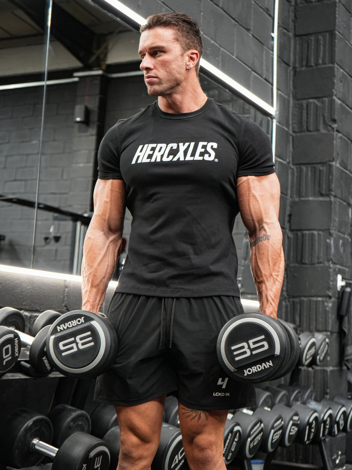 Athlete holding dumbbells in a black fitted HERCXLES muscle tee in the gym