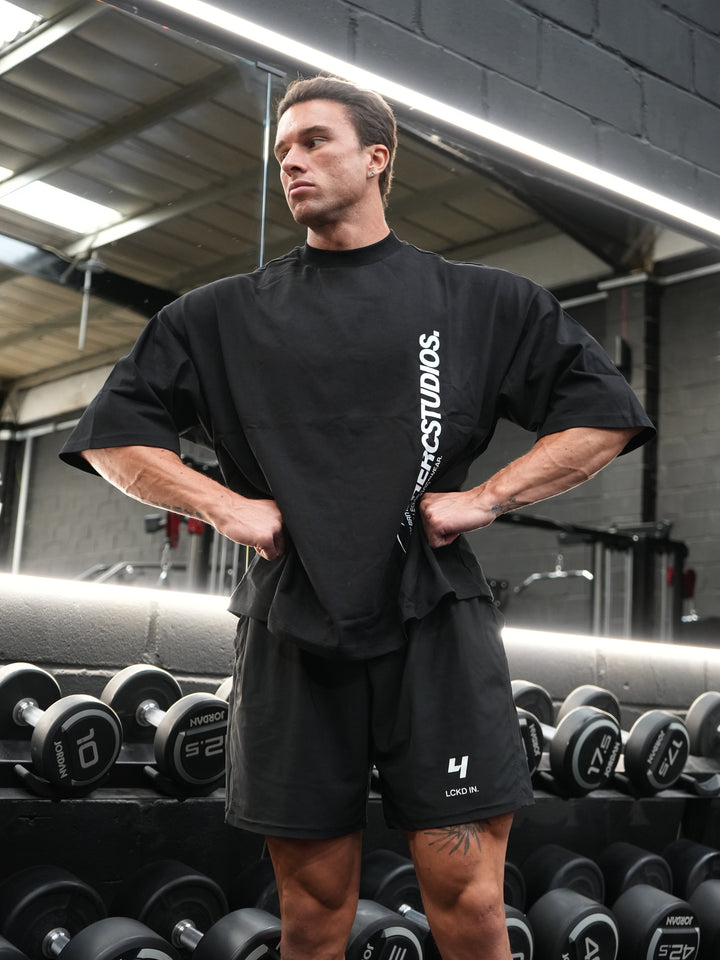 Athlete wearing a black oversized HERCSTUDIOS T-shirt and shorts in a gym