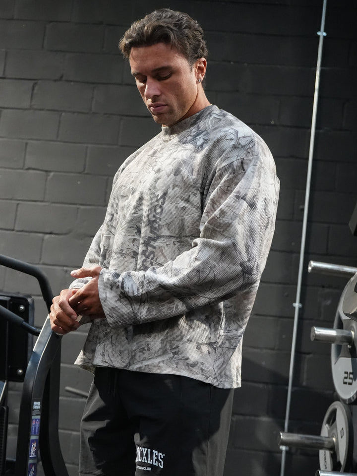 Athlete wearing a grey HERCSTUDIOS camouflage long-sleeve top and black HERCXLES shorts in the gym